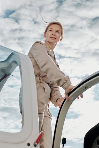 A woman in a flight suit stands in the cockpit of a small plane.