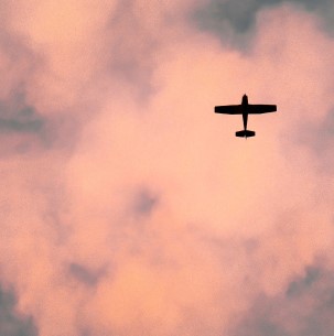 Silhouette of a flying propellor plane against a pink, cloudy sky.